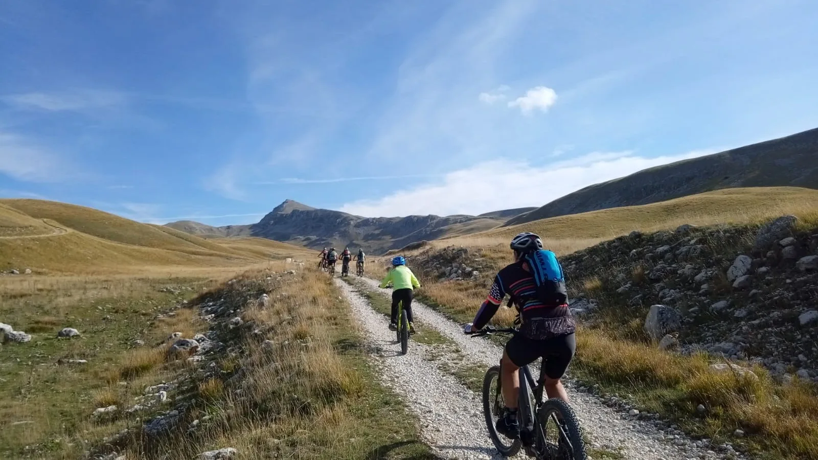 Cicloescursionisti del CAI in mountain bike sull'Altopiano delle Cinque Miglia con vista sul Lago Pantaniello.