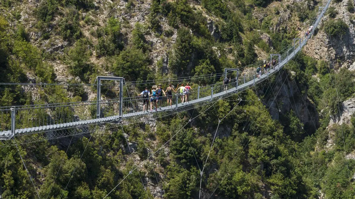 Escursionisti del CAI attraversano il Ponte Tibetano di Castelsaraceno con il Monte la Spina sullo sfondo.