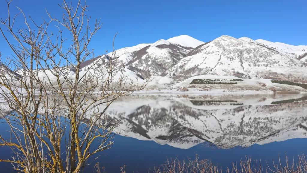 Panorama invernale del Lago del Matese ghiacciato con le montagne innevate sullo sfondo.