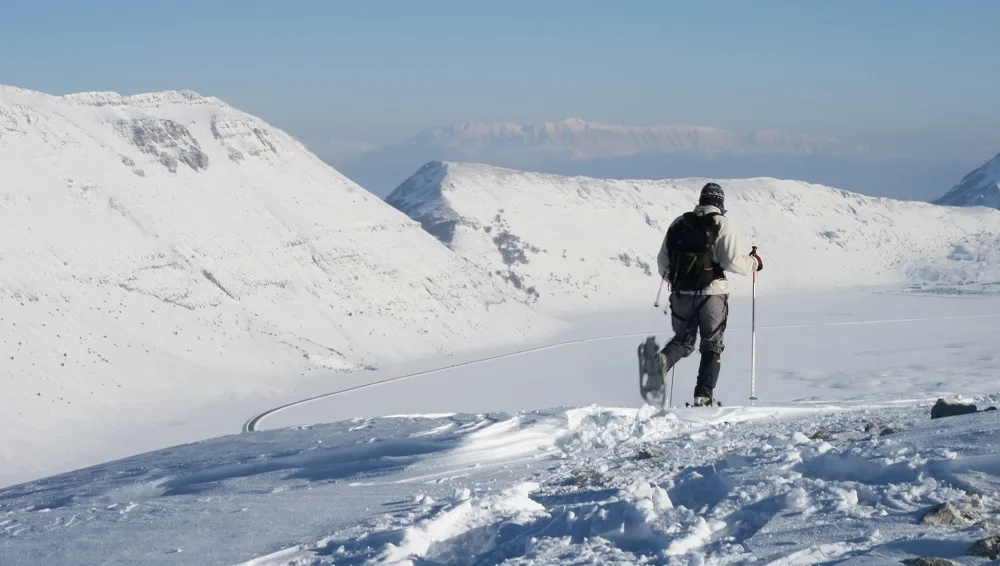 Escursionista con ciaspole e racchette da neve cammina su un pendio innevato del Monte Orsello.